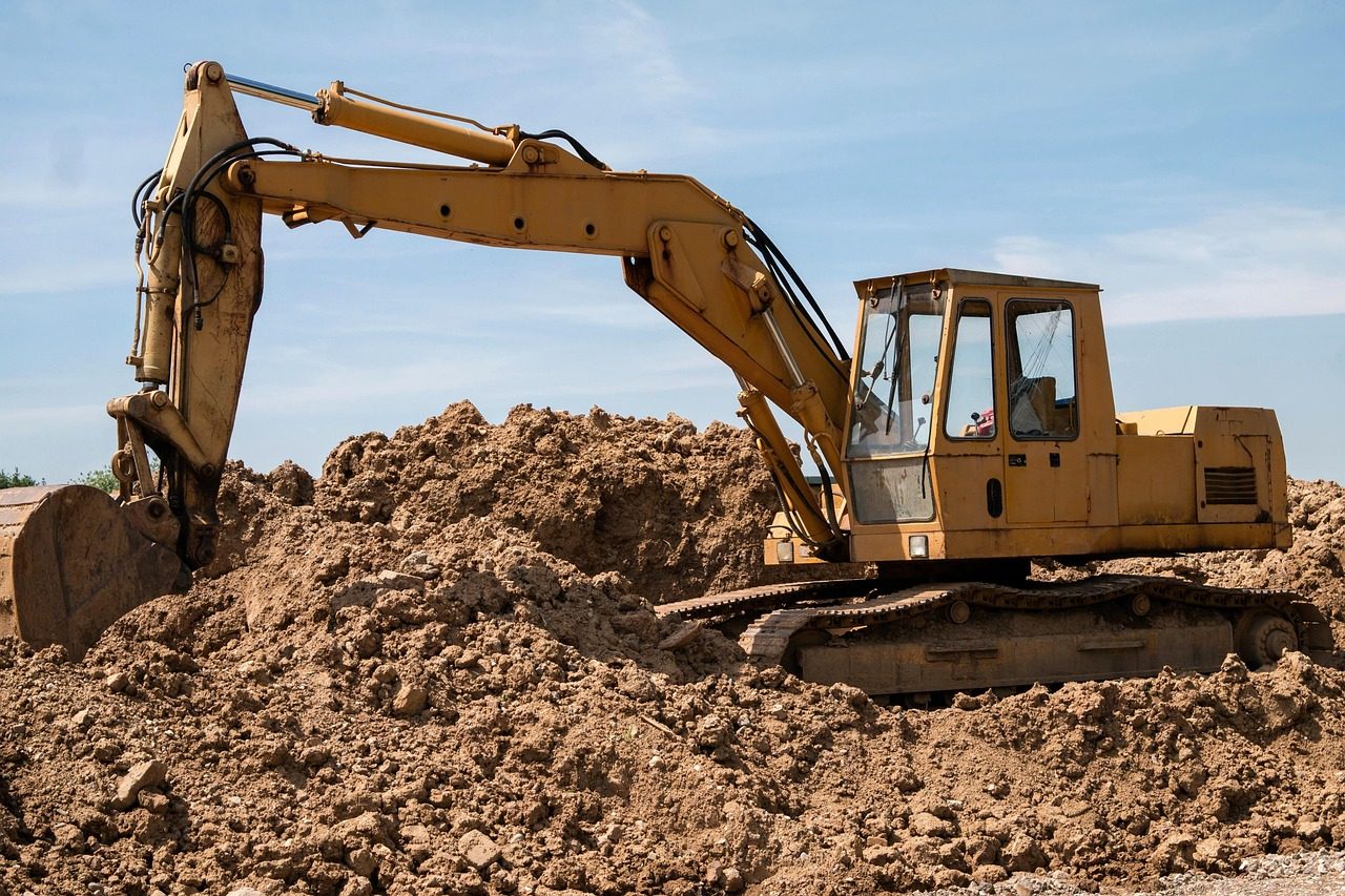 Yellow excavator sitting on a pile of bare soil under a blue sky (sample photo)