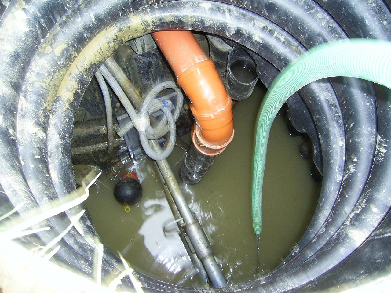 Looking down into a dark round tank with an orange pipe, a green hose and standing water (sample photo)